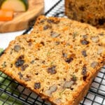 Zucchini Carrot Bread on a baking rack with carrots and zucchini pieces in the background.