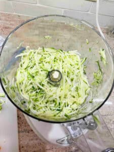 Shredded zucchini in the bowl of the food processor