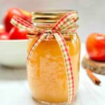 A mason jar filled with applesauce. A bowl of apples is in the background.