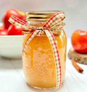 A mason jar filled with applesauce. A bowl of apples is in the background.