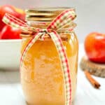 A mason jar filled with applesauce. A bowl of apples is in the background.