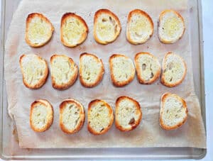 Toasted crostini rounds on a metal cookie sheet.