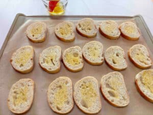 Baguette slices on a metal cookie sheet. They are brushed with olive oil.