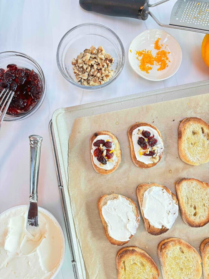 Cranberry crostini on a baking sheet in various stages of preparation.