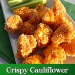 A white platter with cauliflower coated with buffalo sauce and breadcrumbs that have been roasted. Celery Sticks in the background