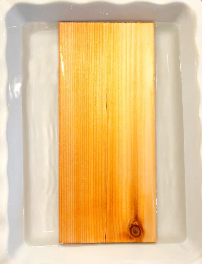 A cedar plank soaking in water in a white casserole