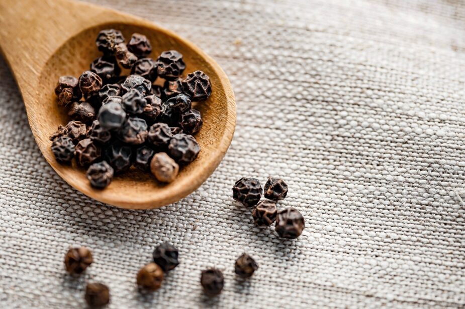 Black peppercorns in a wooden spoon and on a beige woven tablecloth
