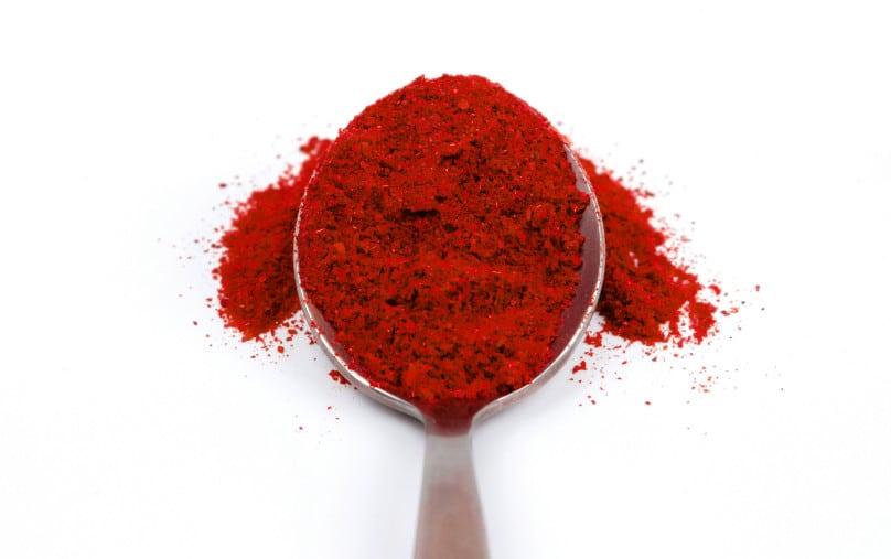 A metal spoon filled with cayenne pepper on a white background