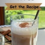 A clear glass of iced coffee with cinnamon sticks in the background