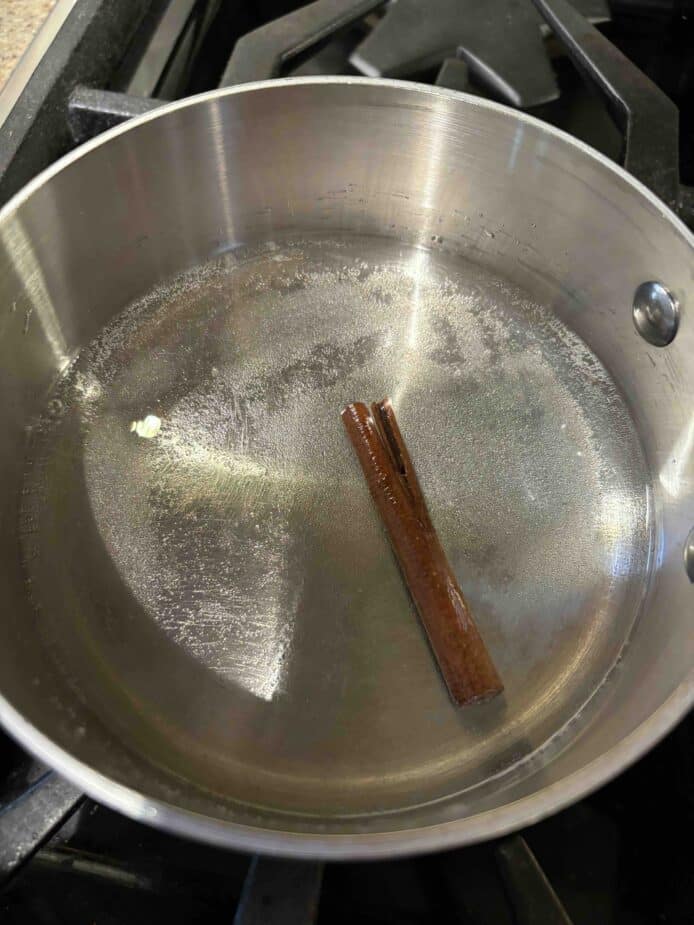 A sauce pan with water and sugar and a cinnamon stick cooking on the stove.
