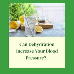 A water glass on a marble table with a sliced lemon and greenery in the background. The title: Can Dehydration Increase Your Blood Pressure is directly below the picture.