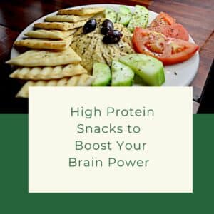 A plate of hummus with cut vegetables and flatbread around it. The title - High Protein Snacks to Boost Your Brain Power is in a box below.