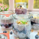 4 jars of lemon blueberry chia pudding on a white table in front of a sunny window.