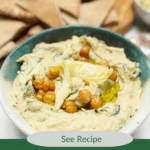 Spinach and artichoke hummus in a green and white ceramic bowl with pita wedges in the background