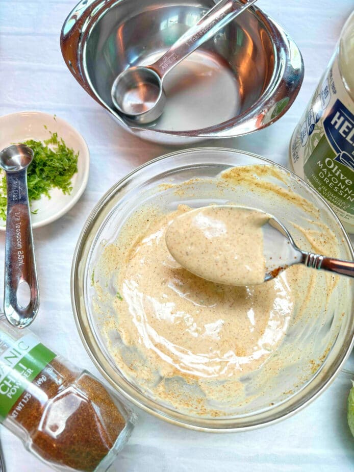 Mayonnaise based dressing with chili powder mixed in, in a small glass bowl. A spoon is lifting some of the dressing out of the bowl.