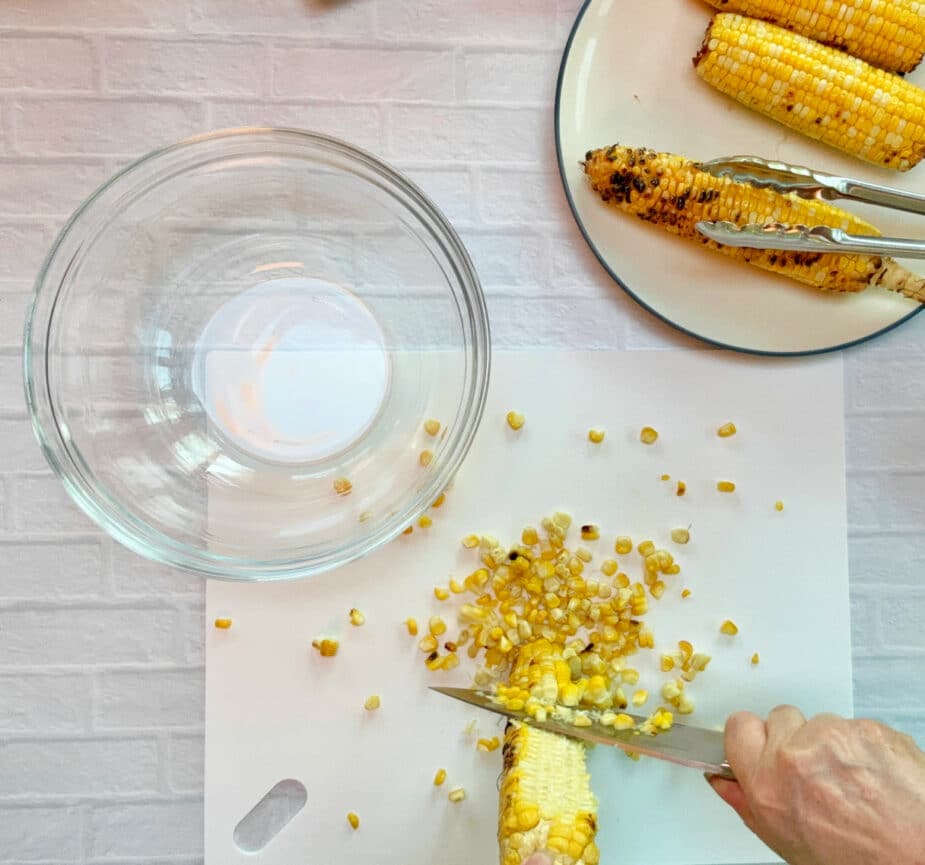 Cutting corn off the cob onto a cutting board