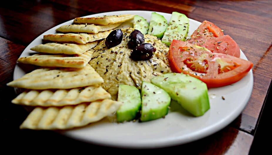 Hummus on a white plate surrounded by cut vegetables and pita bread