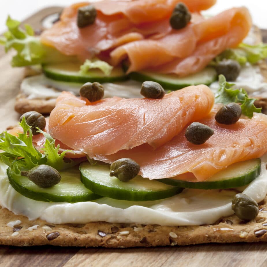 Smoked salmon on thin slices of cucumber on a smear of goat cheese on a whole grain cracker. Capers are sprinkled over top