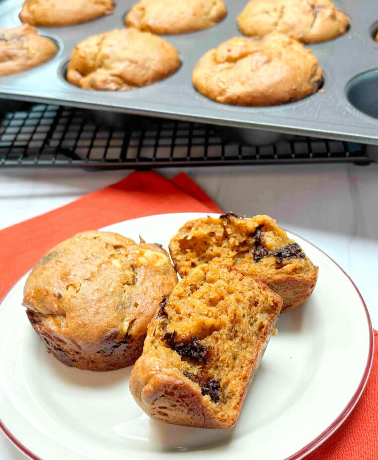 Banana Peanut Butter Muffins on a white plate with a muffin tin with baked muffins in the background.