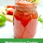 A watermelon and lime cooler in a clear ball jar glass on a red placemat on a white picnic table.