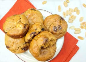 A plate of Banana Peanut Butter Chocolate Chip Muffins on an orange napkin