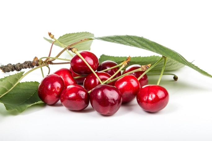 A pile of cherries with their leaves and stems on a white table top