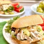 Chicken Salad with grapes and almonds on a ciabatta roll with watermelon slices and salad next to it.