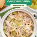 Chicken salad with green grapes and almonds in a white bowl on a marble counter. A bowl of grapes is on the side.