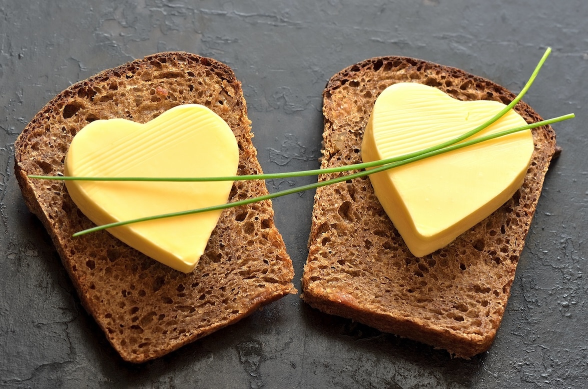 Two slices of whole grain bread with heart shaped margarine in the middle of each slice topped with chives