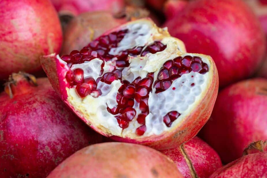 An open pomegranate showing the seeds on top of a pile of fresh pomegranate fruits