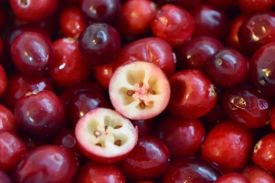 A pile of fresh cranberries with one cut open to show the detail of the inside