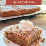 A square piece of apple spice cake with a dollop of whipped cream on a white plate, sprinkled with walnuts and cinnamon sugar