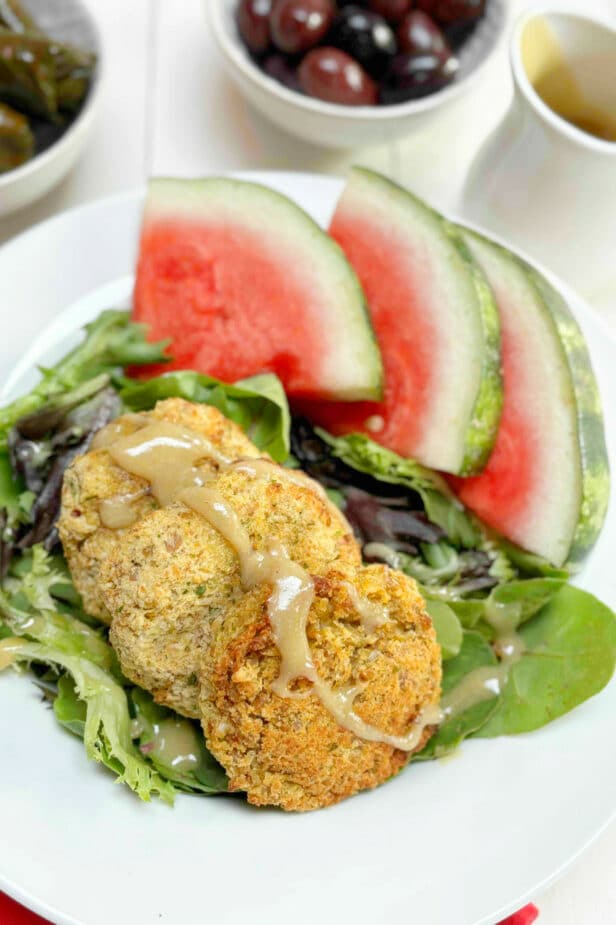 Baked falafels on a green salad with sliced watermelon, stuffed grape leaves and olives in the background