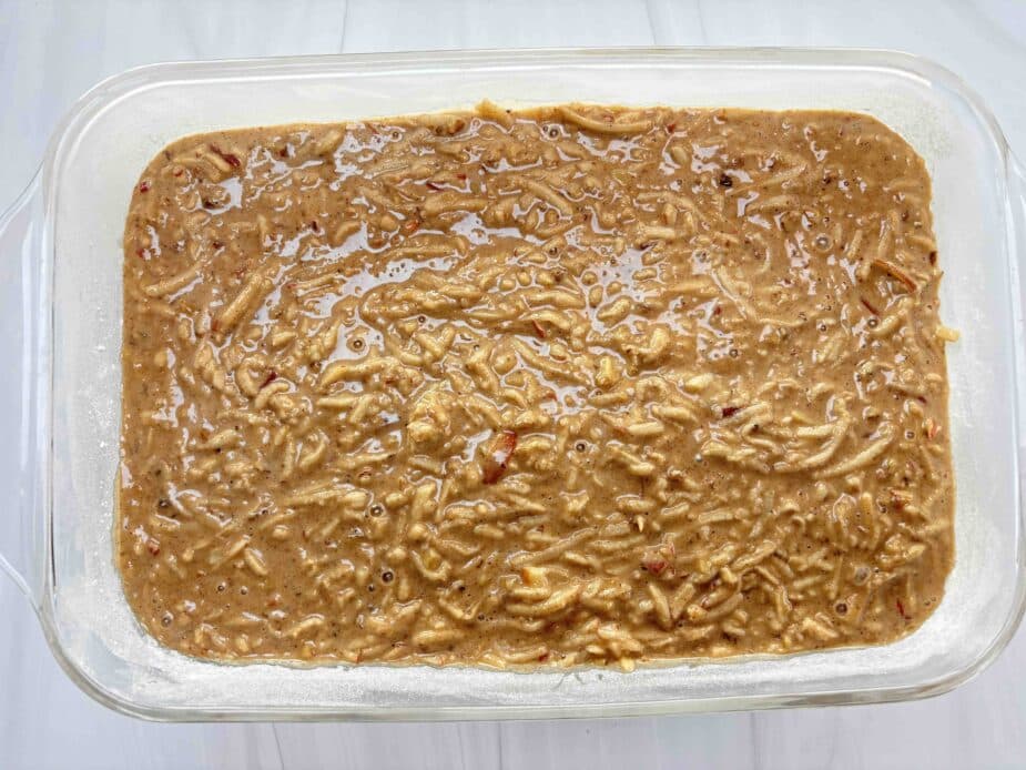 The apple spice cake batter in a prepared glass cake pan on a marble counter before baking.