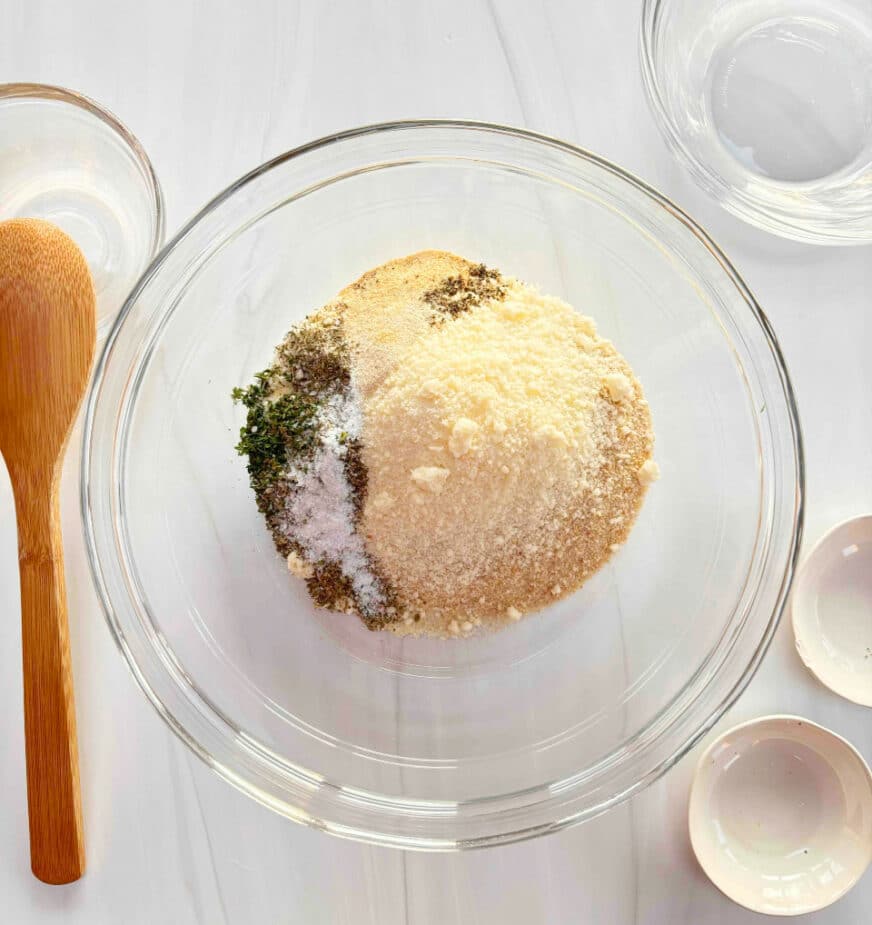 Breadcrumbs, parmesan cheese, herbs and spices in a glass bowl on a marble counter