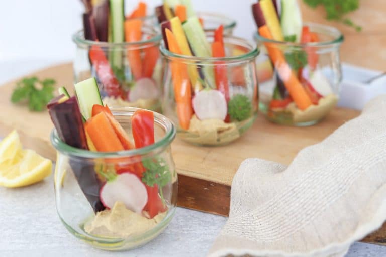 Glass cups with a little hummus in the bottom and sliced veggies filling the cup.