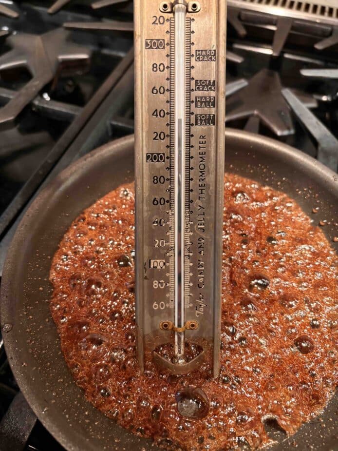 Maple syrup boiling in a non stick pan with a candy thermometer indicating it has reached 235°F.