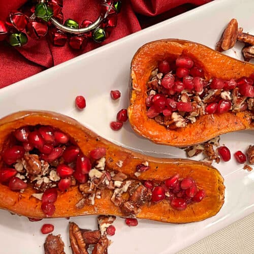 Two roasted honeynut squash halves filled with pomegranate seeds and candied pecans on a white serving platter.