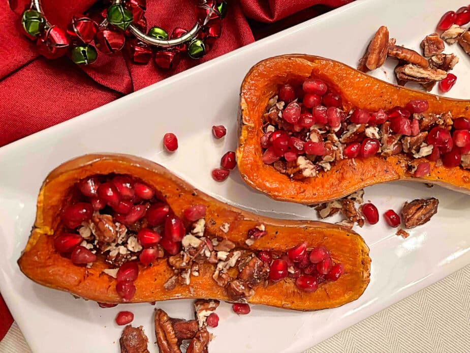 Two roasted honeynut squash halves filled with pomegranate seeds and candied pecans on a white serving platter.