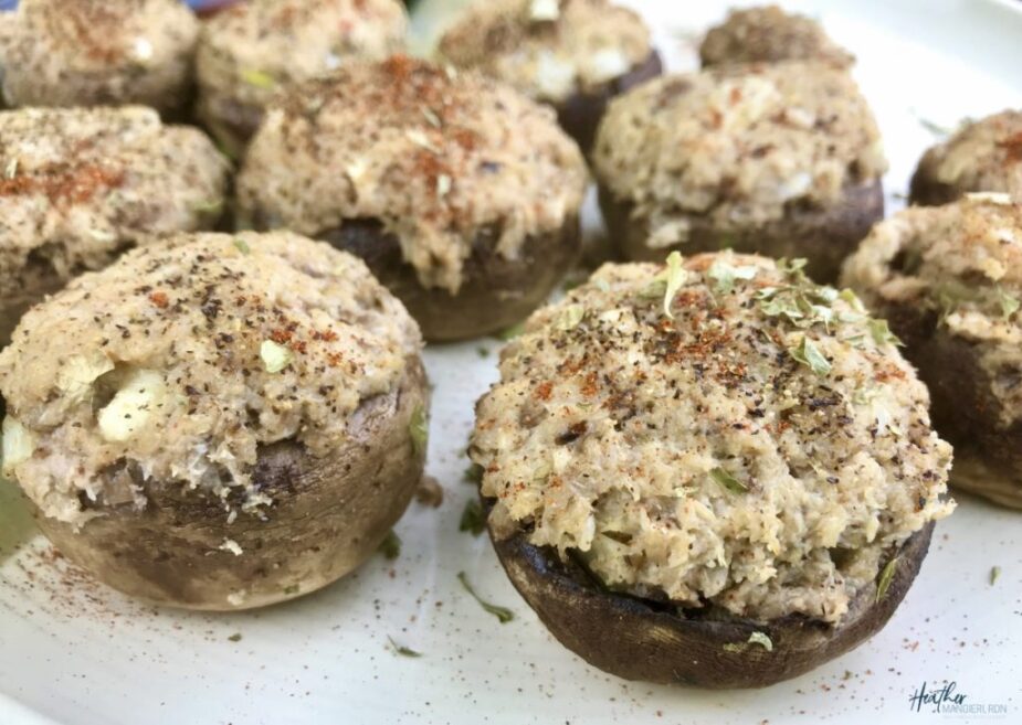 Mushroom caps stuffed with a creamy crab filling on a white platter. The mushrooms are sprinkled with paprika and herbs.