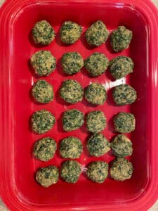 A red casserole dish filled with spinach balls