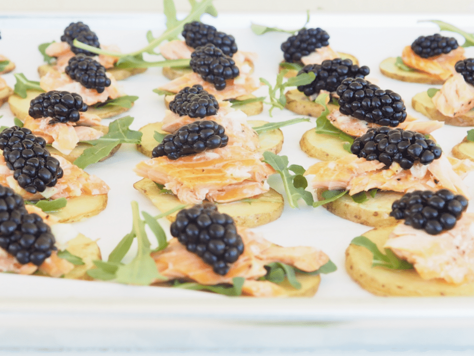 Slices of yellow potatoes topped with arugula, artic char (seafood like salmon) and a blackberry