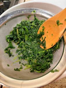 Cooked chopped frozen spinach draining in a mesh strainer over a white bowl 