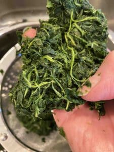 Chopped spinach that has been squeezed dry held over a strainer