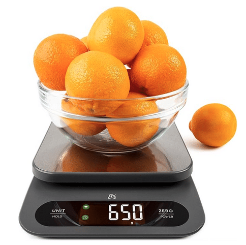 A digital food scale with a bowl of oranges on top with the weight of 65.0 showing on the display