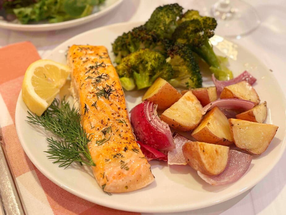 A salmon fillet, roasted red potatoes, and broccoli on a white plate.