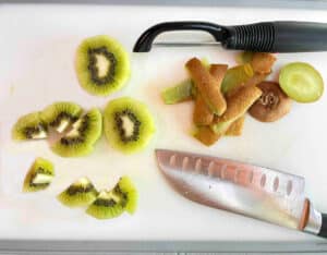 Peeled and cut kiwi fruit on a white cutting board.